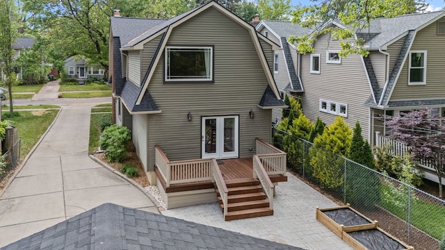 rear view of property with a gambrel roof, a chimney, a deck, french doors, and a fenced backyard