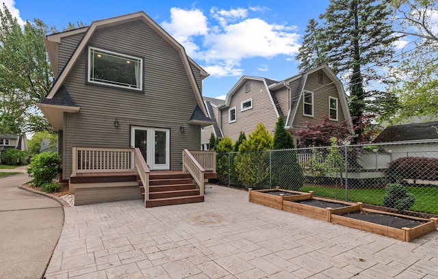 back of property featuring a gambrel roof, a garden, a deck, and a patio