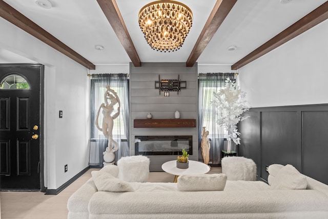 living room featuring a chandelier, beamed ceiling, wood finished floors, a decorative wall, and baseboards