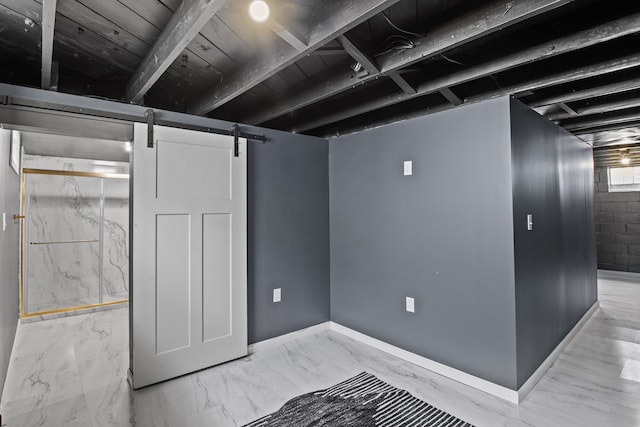 finished basement featuring a barn door, baseboards, and light marble finish flooring