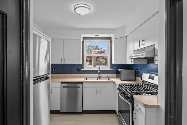kitchen featuring stainless steel appliances, under cabinet range hood, a sink, light countertops, and white cabinets