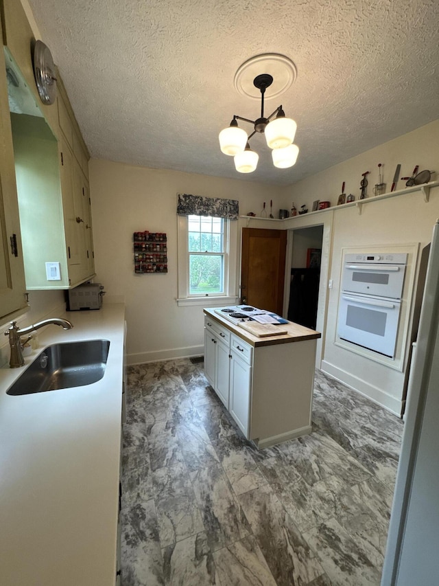 701 Chestnut St, Grayling, MI 49738 - kitchen featuring a sink, a chandelier, a textured ceiling, white appliances, and baseboards