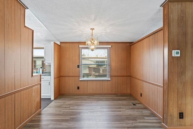 25 Hunters Rill, Lapeer, MI 48446 - unfurnished dining area featuring wood finished floors, a chandelier, wooden walls, and a textured ceiling