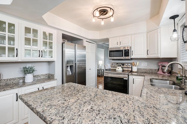 kitchen featuring appliances with stainless steel finishes, a sink, white cabinetry, light stone countertops, and glass insert cabinets