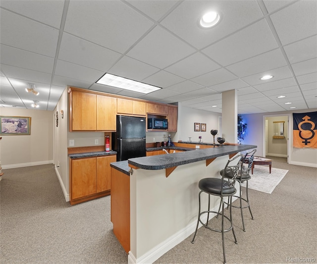 17747 Parkshore Dr, Northville, MI 48168 - kitchen featuring black appliances, light colored carpet, dark countertops, a kitchen breakfast bar, and a paneled ceiling