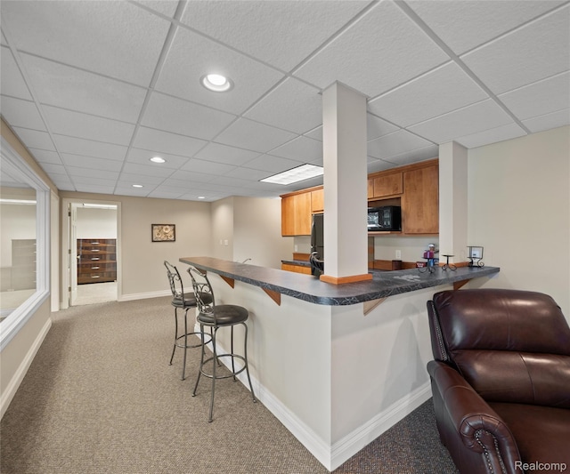 17747 Parkshore Dr, Northville, MI 48168 - kitchen with carpet floors, a breakfast bar area, dark countertops, a paneled ceiling, and a peninsula