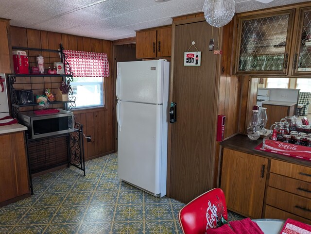 5268 S Arrowhead Trl, Baldwin, MI 49304 - kitchen with freestanding refrigerator, stainless steel microwave, brown cabinets, tile patterned floors, and wood walls