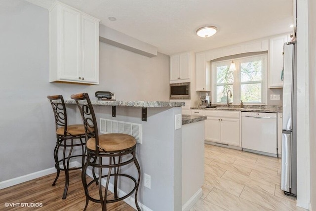 2553 Bristol Ter, Saint Joseph, MI 49085 - kitchen with appliances with stainless steel finishes, light stone counters, white cabinetry, a breakfast bar, and a sink