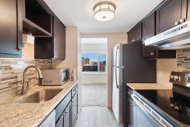 555 E William St Unit 10D, Ann Arbor, MI 48104 - kitchen with stainless steel appliances, a sink, under cabinet range hood, dark brown cabinets, and decorative backsplash