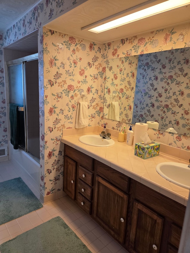full bath with double vanity, tile patterned floors, wallpapered walls, a shower with door, and baseboards