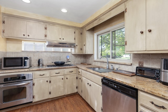 935 S Brys Dr, Grosse Pointe Woods, MI 48236 - kitchen featuring stainless steel appliances, under cabinet range hood, a sink, dark wood-style floors, and decorative backsplash