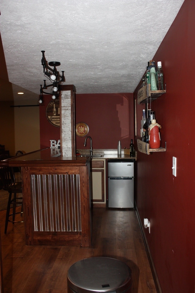 indoor bar with freestanding refrigerator, a textured ceiling, and dark wood-type flooring