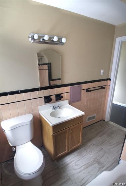 15470 Mapleridge St, Detroit, MI 48205 - bathroom with tile walls, vanity, toilet, and a wainscoted wall