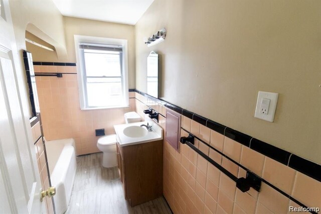 15470 Mapleridge St, Detroit, MI 48205 - bathroom with tile walls, toilet, vanity, a wainscoted wall, and a tub to relax in