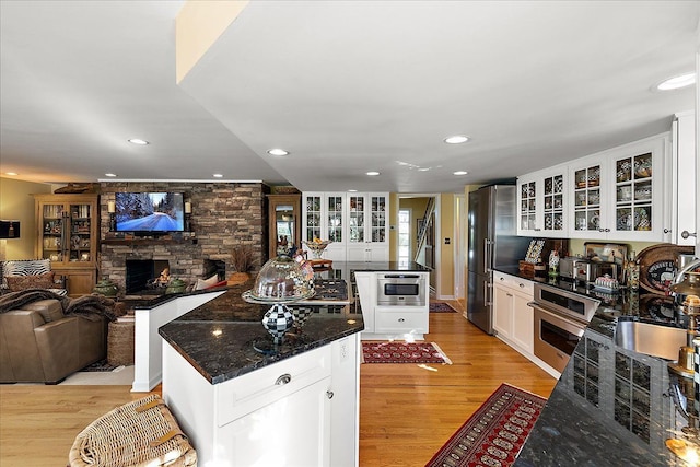 1301 Fairway Dr, Birmingham, MI 48009 - kitchen featuring appliances with stainless steel finishes, a center island, a stone fireplace, light wood finished floors, and white cabinets