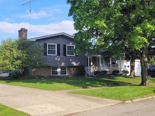 tri-level home featuring a front yard, a chimney, a porch, and brick siding