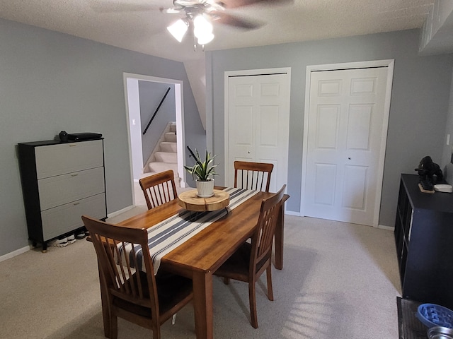 dining space featuring ceiling fan, light colored carpet, stairs, and baseboards