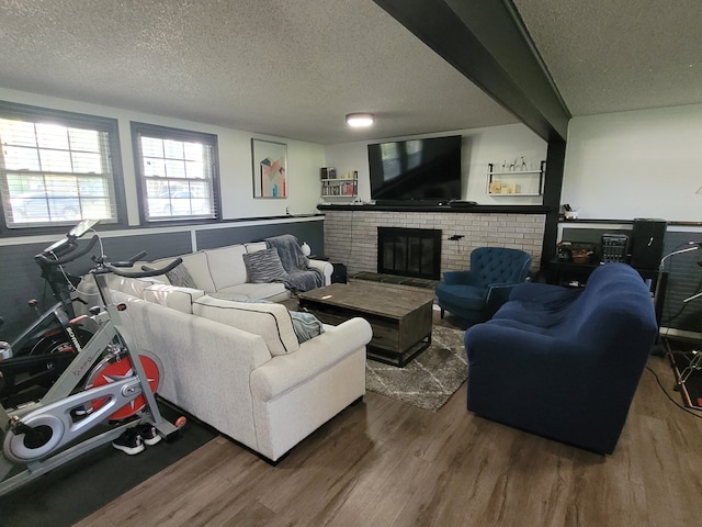 living room featuring wood finished floors, a textured ceiling, and a brick fireplace