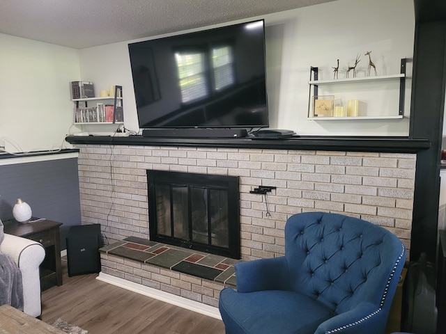 living area featuring wood finished floors, a brick fireplace, and a textured ceiling