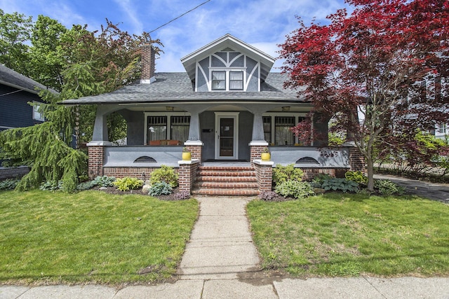 view of front of property featuring a porch, a front yard, a chimney, and stucco siding
