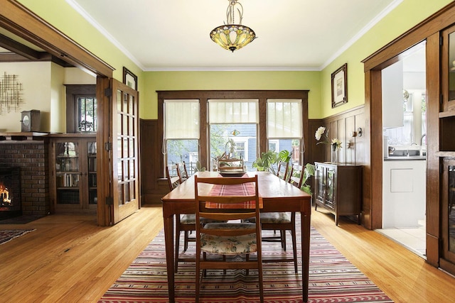 dining space featuring ornamental molding, healthy amount of natural light, light wood finished floors, a brick fireplace, and wainscoting