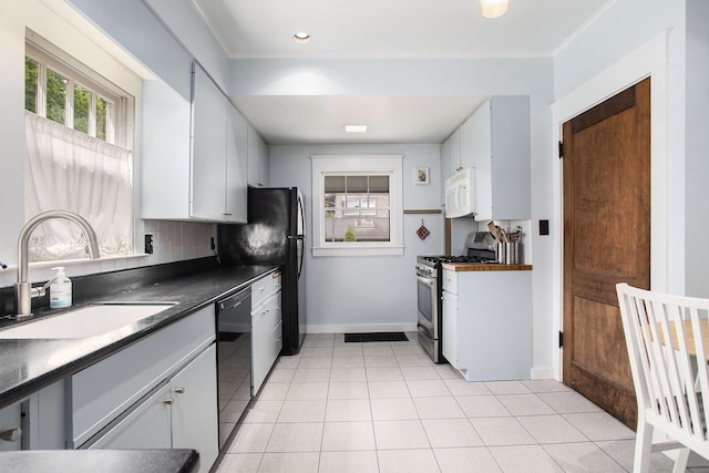 kitchen with gas range, white microwave, a sink, black dishwasher, and dark countertops