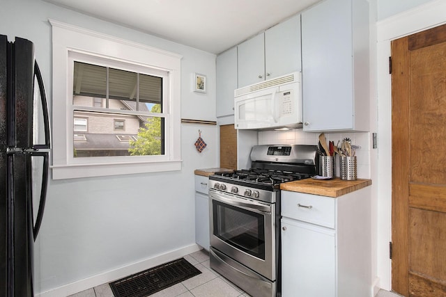 kitchen featuring white microwave, stainless steel range with gas stovetop, freestanding refrigerator, light tile patterned floors, and decorative backsplash