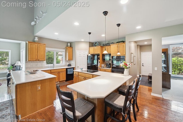 921 Gleneagles, Highland, MI 48357 - kitchen featuring black appliances, a sink, wood finished floors, decorative backsplash, and a kitchen island with sink