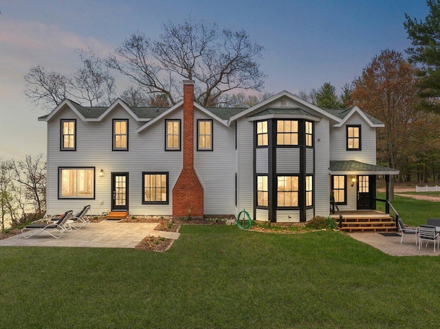 8282 W Harrison Rd, Mears, MI 49436 - back of house at dusk with a chimney, a patio, a yard, and a shingled roof