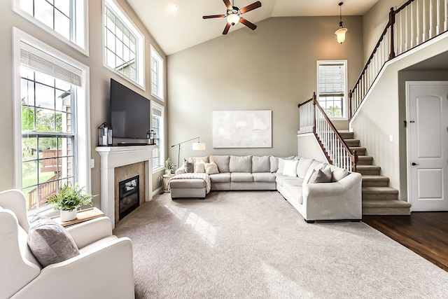 58799 Carriage Ln, South Lyon, MI 48178 - living room featuring ceiling fan, high vaulted ceiling, a tiled fireplace, stairs, and dark wood-style floors