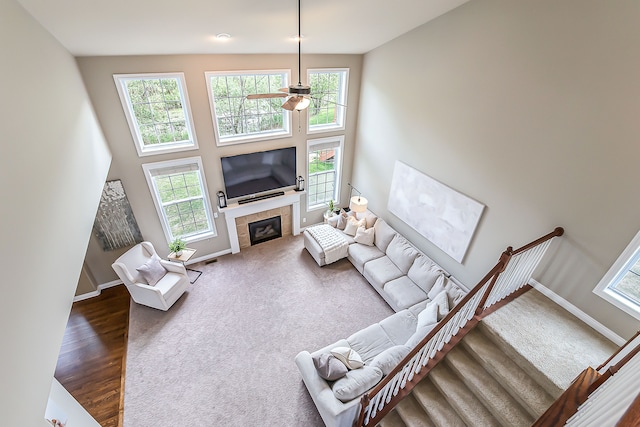 58799 Carriage Ln, South Lyon, MI 48178 - carpeted living room featuring ceiling fan, a tiled fireplace, baseboards, a towering ceiling, and wood finished floors