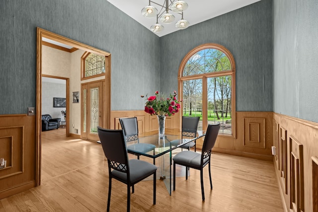 9997 Applegate Ln, Brighton, MI 48114 - dining area with wallpapered walls, light wood-style flooring, a wainscoted wall, a chandelier, and a towering ceiling