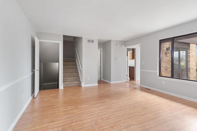 empty room with light wood-type flooring, stairs, and baseboards