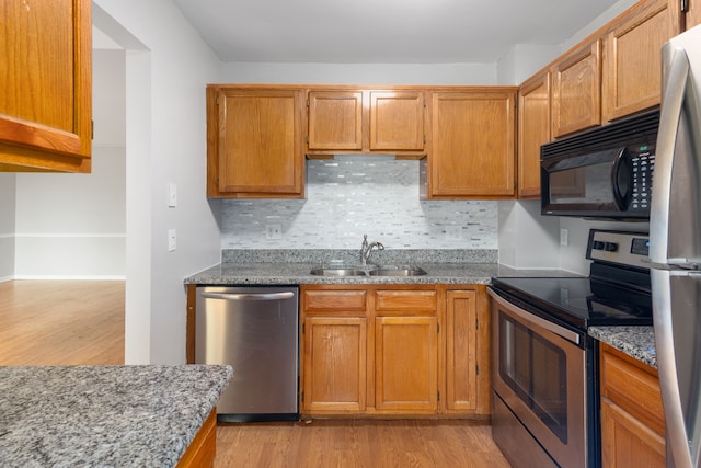 kitchen with stainless steel appliances, a sink, light wood finished floors, decorative backsplash, and light stone countertops