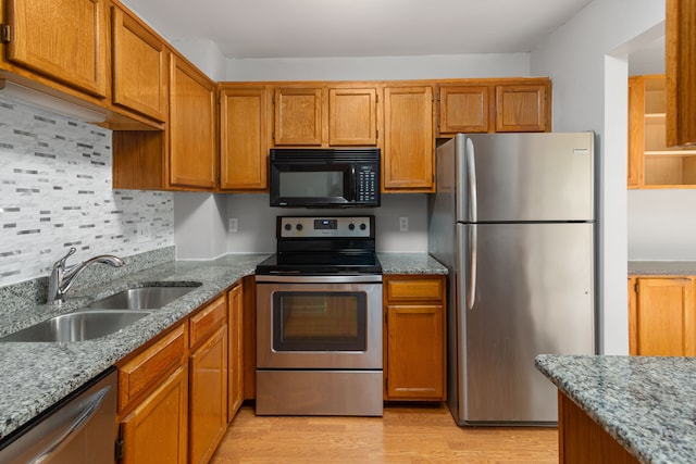 kitchen with stainless steel appliances, a sink, light wood-type flooring, and light stone counters