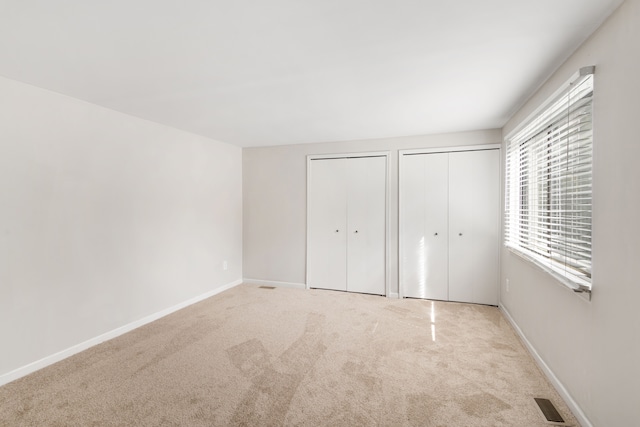 unfurnished bedroom featuring two closets, carpet flooring, and baseboards