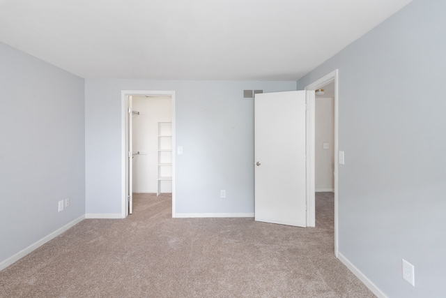 unfurnished bedroom featuring carpet floors, a walk in closet, and baseboards
