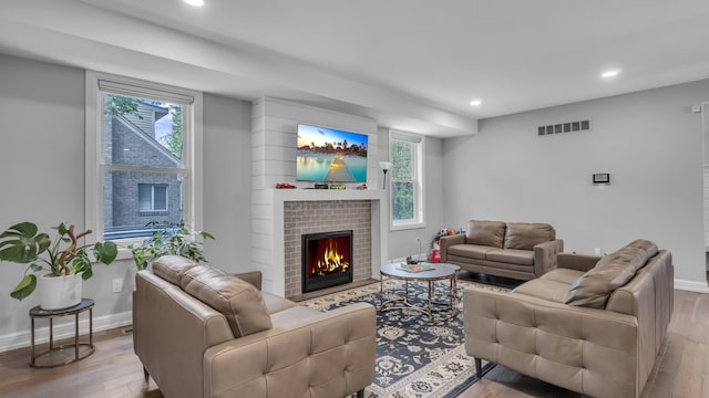 living room featuring recessed lighting, wood finished floors, a warm lit fireplace, and baseboards