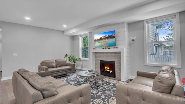 living room featuring a warm lit fireplace, wood finished floors, recessed lighting, healthy amount of natural light, and baseboards