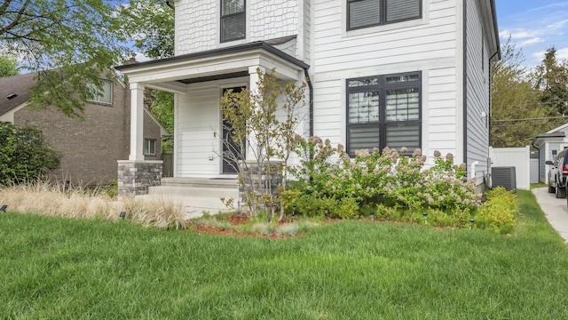 view of exterior entry featuring central AC, a yard, and covered porch