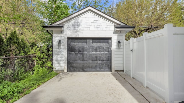 detached garage featuring fence, driveway, and a gate