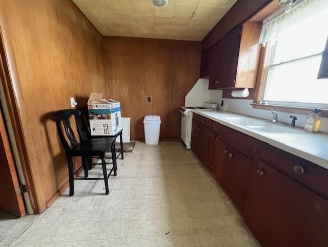 205 Evans St, East Tawas, MI 48730 - kitchen with stove, a sink, light countertops, wood walls, and light flooring