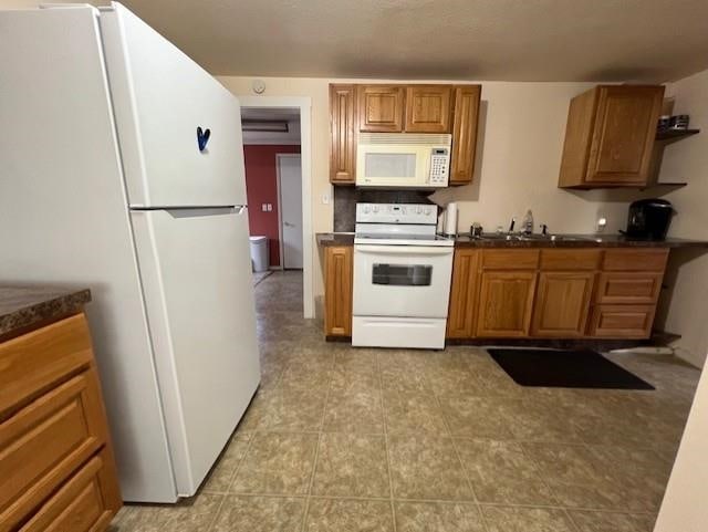 205 Evans St, East Tawas, MI 48730 - kitchen featuring white appliances, dark countertops, brown cabinets, light tile patterned floors, and decorative backsplash
