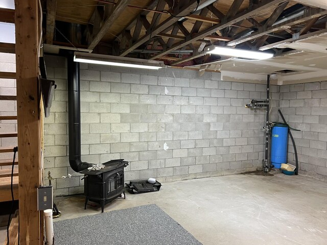 8711 M-37, Irons, MI 49644 - unfinished below grade area featuring a wood stove, concrete block wall, and a water pressure tank