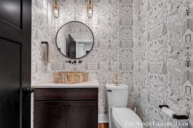 half bathroom with wallpapered walls, toilet, and vanity