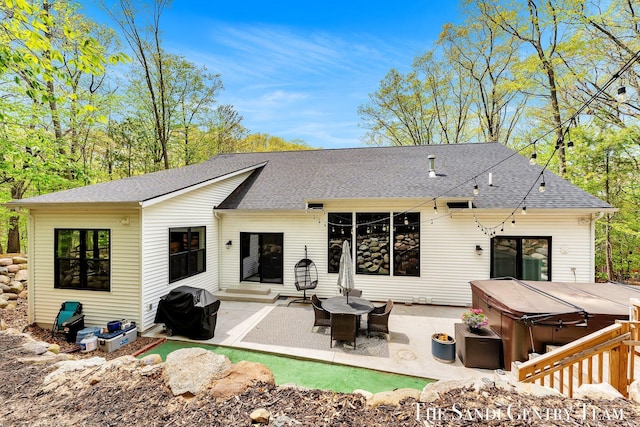 rear view of house with a hot tub, a patio area, and a shingled roof