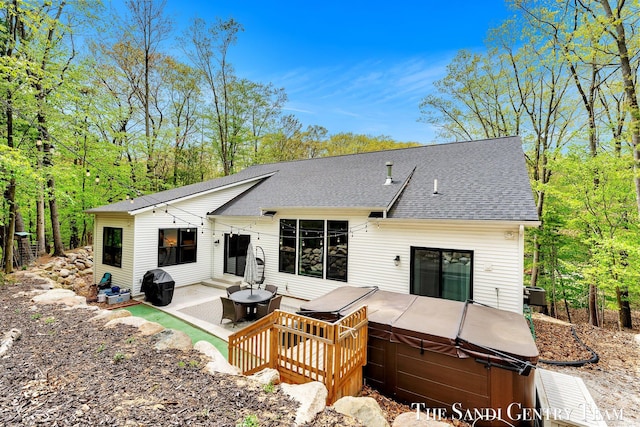 back of house featuring a hot tub, roof with shingles, a wooden deck, and a patio area