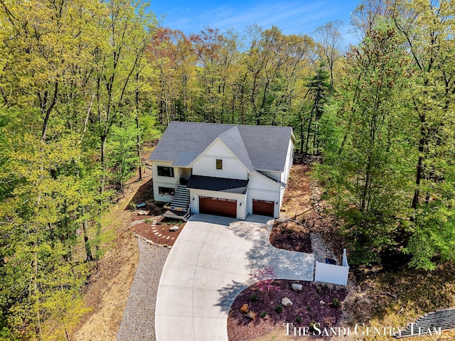 view of front of house featuring concrete driveway, board and batten siding, an attached garage, roof with shingles, and a wooded view