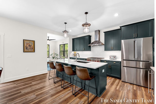 kitchen with freestanding refrigerator, wall chimney exhaust hood, a sink, wood finished floors, and a breakfast bar area