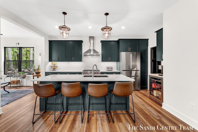 kitchen featuring wall chimney range hood, freestanding refrigerator, a sink, light countertops, and a kitchen breakfast bar